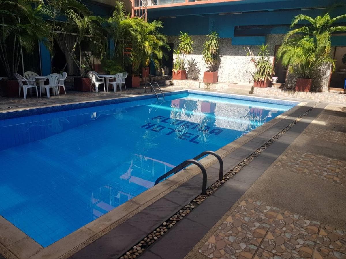 An outdoor swimming pool edged with palm trees and white poolside chairs.
