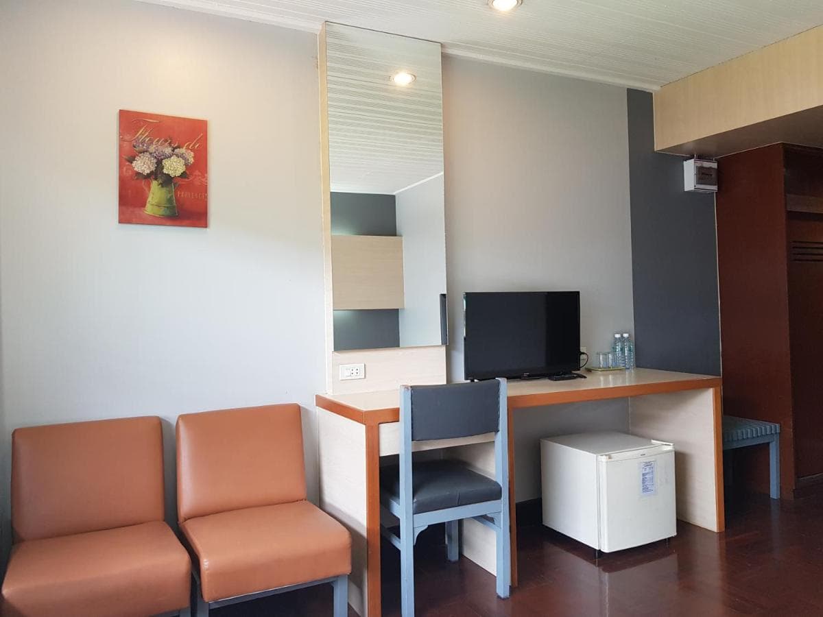 A guest room desk with a mirror, television, refrigerator and two armchairs.