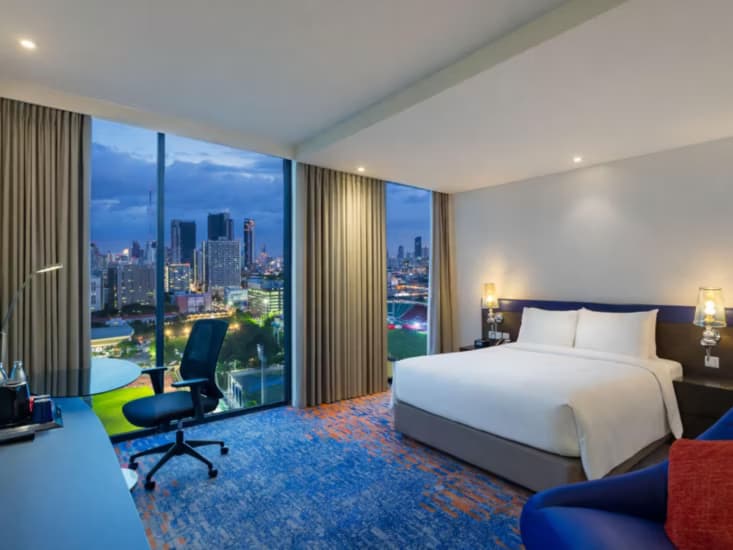 A king room with a corner window looking over the city at dusk.
