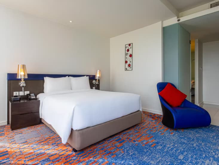 A king room with a red and blue lounge chair beside the bed.
