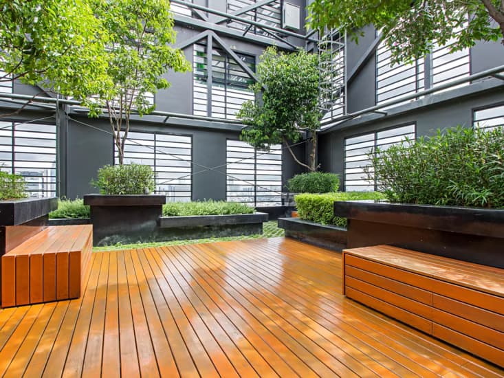 A rooftop garden with a timber deck, benches and planted trees.
