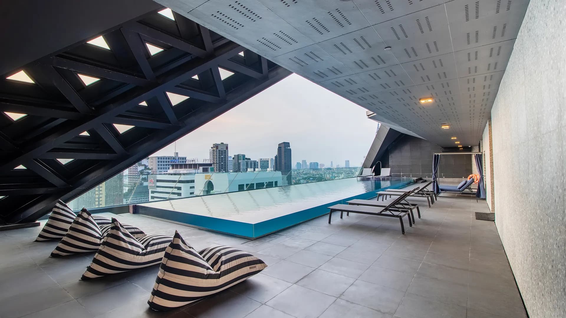 Sun loungers on the pool deck beneath the building's angular concrete frame.