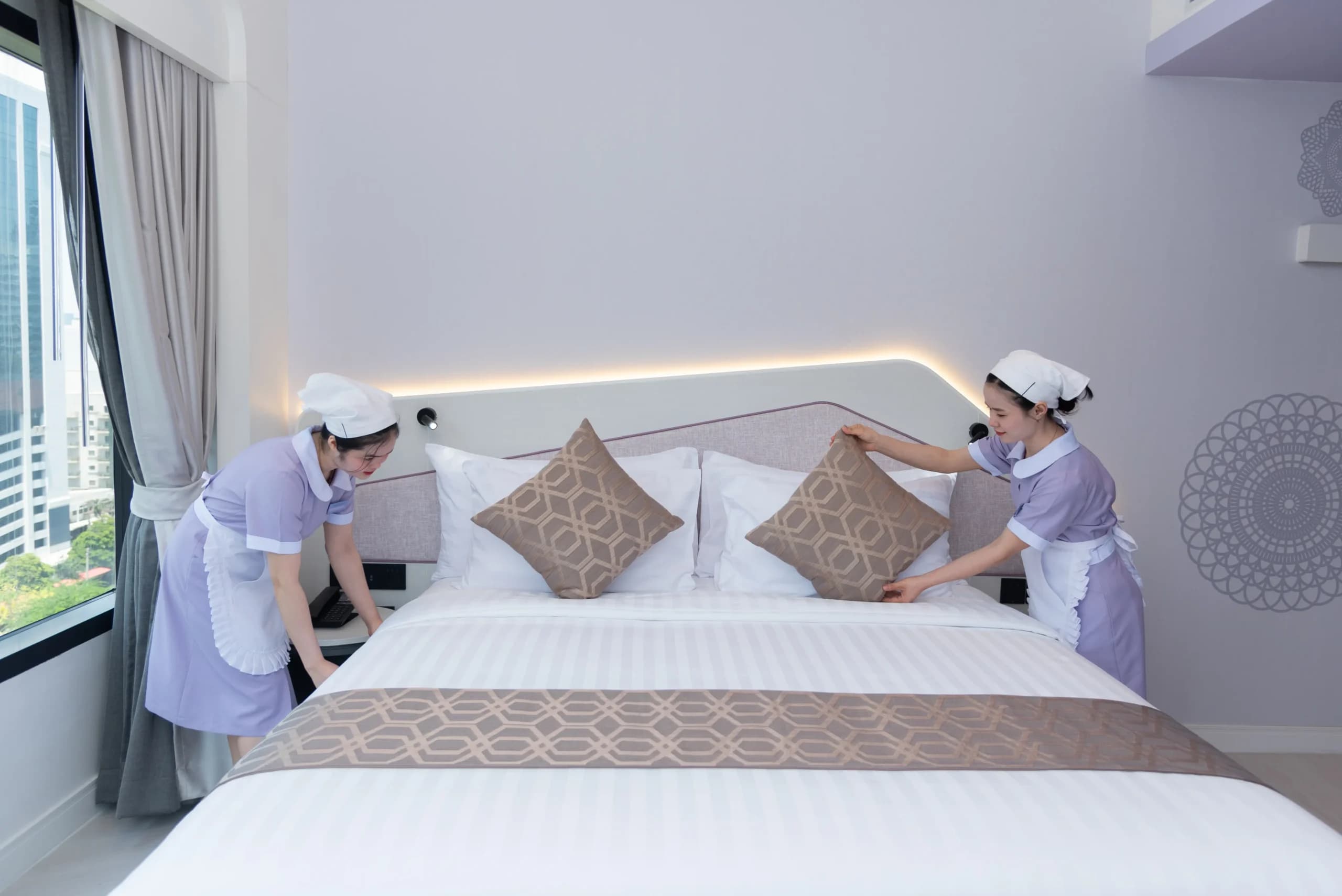 Two housekeepers making up a bed in a guest room.