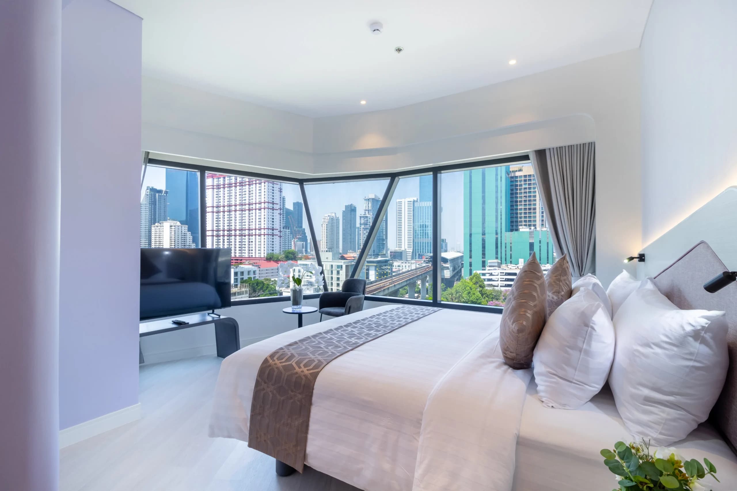 A bedroom with a corner window looking out over the city.