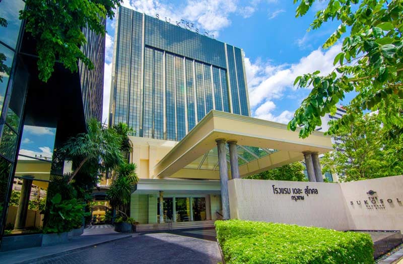 The hotel entrance and glass façade, framed by trees and clipped hedges.