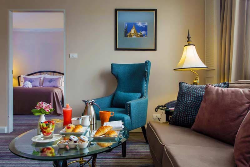A suite living area with breakfast laid on a low table beside a blue armchair.
