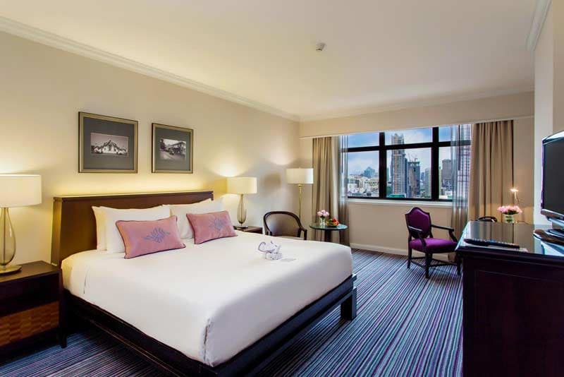 A bedroom with a king bed and a window looking out over the city.