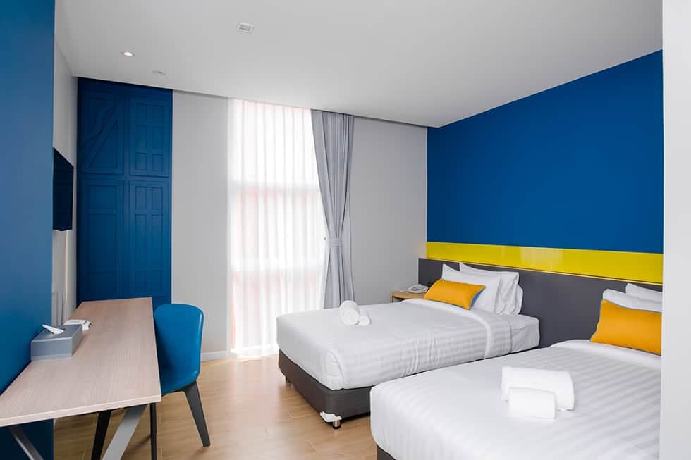A twin room with a blue and yellow accent wall and a corner desk.